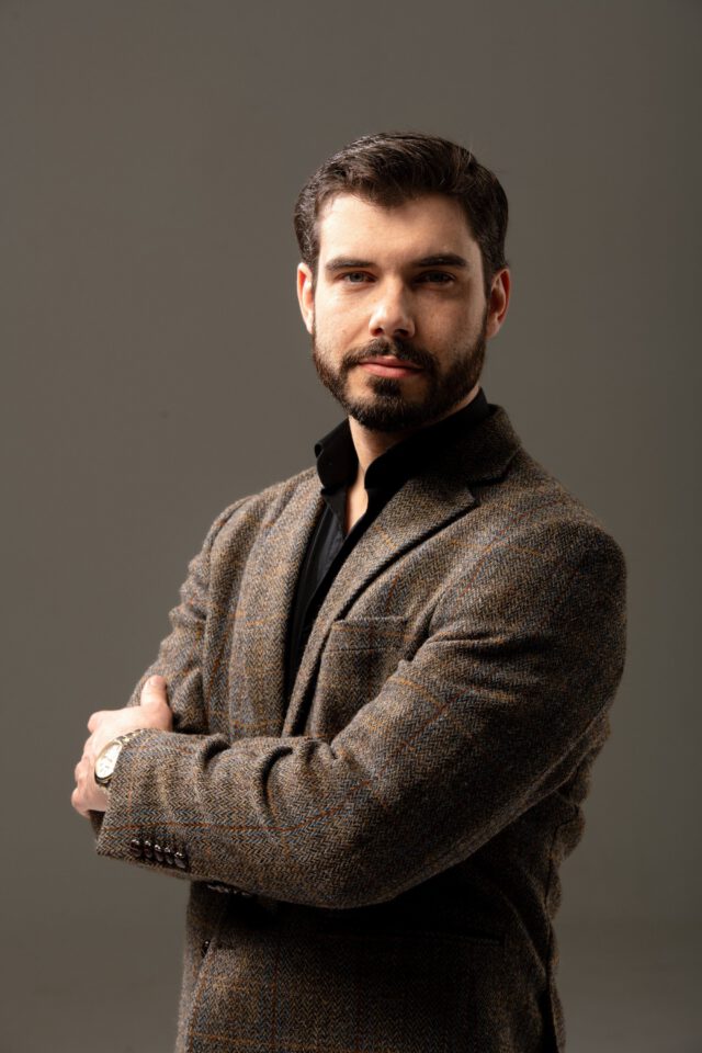 Magnus Lindegård, bearded man in a tweed blazer and black shirt, professional portrait against gray background