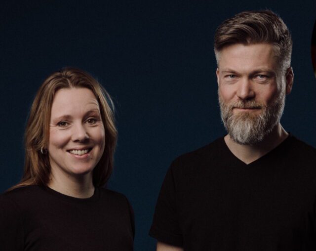 Norbakken and Nystabakk, a woman and bearded man in black shirts, posing against a dark blue background, 2025.